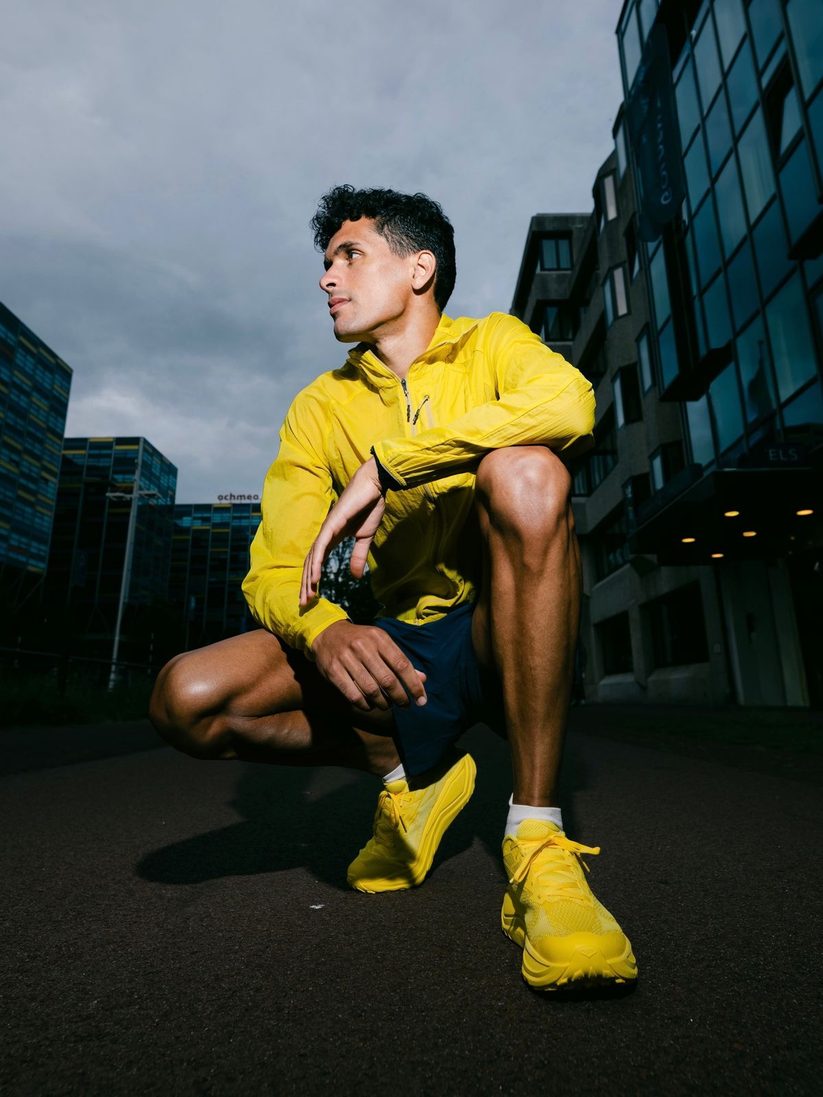 Noah Schutte kneeling in a yellow jacket between glass towers